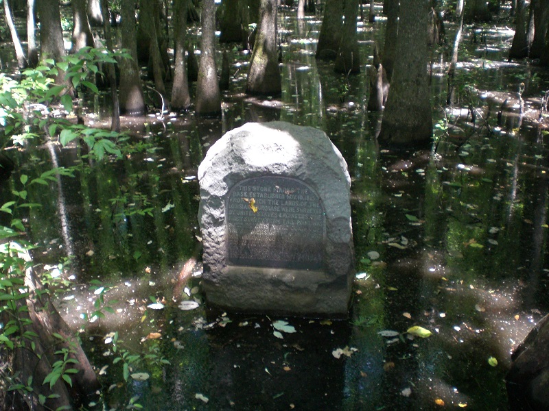 stone with inscription in the middle of a leafy pool, with trees growing out of and reflecting in the water